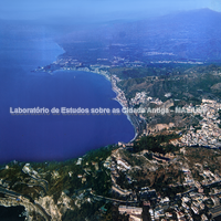 Vista aérea da moderna cidade de Taormina. Vê-se igualmente a cidade de Giardini Naxos e ao fundo o Capo Schisò, local do assentamento da apoikia de Naxos na Antigüidade. Fotografia: Francesco Alaimo